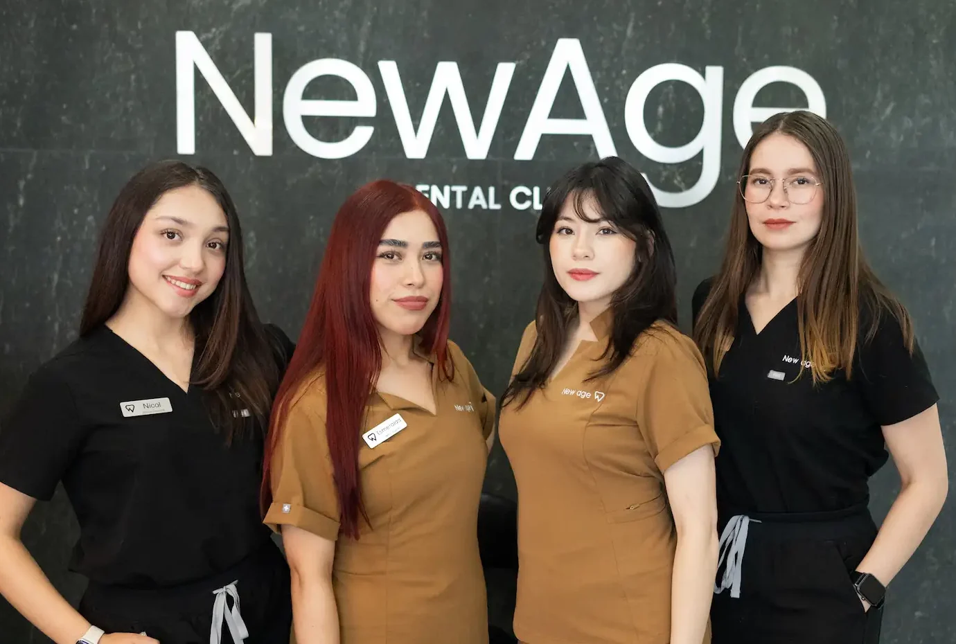 Four women wearing scrubs stand in front of a "New Age Dental Clinic" sign, posing for a group photo.