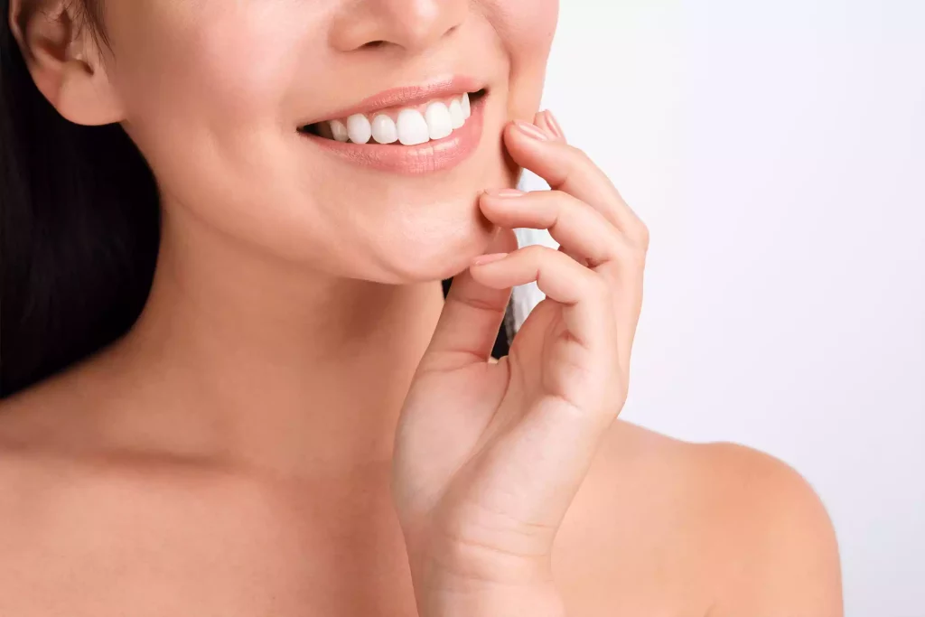 A woman smiling with her hand on her face, showcasing perfect orthodontics.