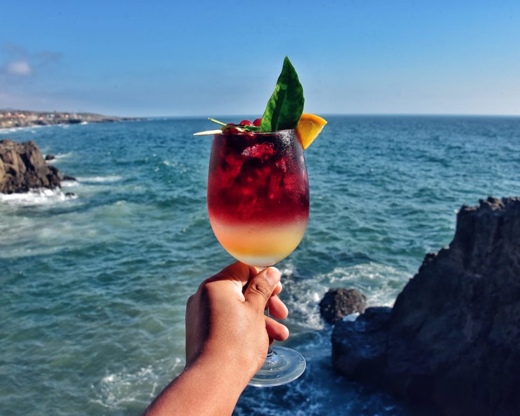 A person holding up a glass of drink near the ocean while visiting the clinic.