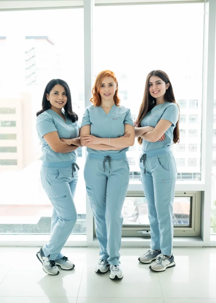 Three women in blue scrubs standing in front of a window at a cosmetic dentistry clinic.