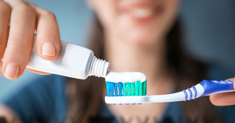 A woman demonstrates one of the 6 ways to improve your smile by holding a toothbrush and toothpaste.
