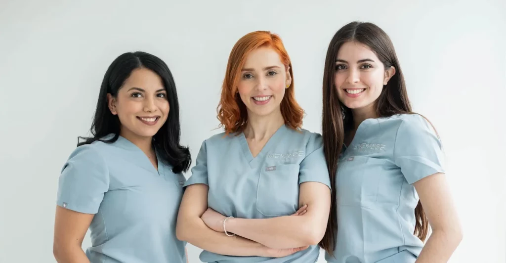 Smile Renewal with New Age Dental: Dental Implant Specialists 3 Three women, who are dental implant specialists, in scrubs posing for a photo.