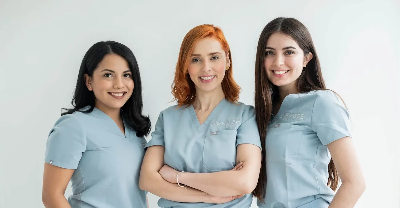 Three women, who are dental implant specialists, in scrubs posing for a photo.