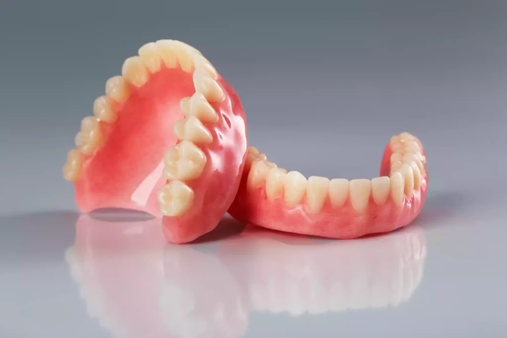 A pair of pink dentures on a grey surface undergoing periodontal cleaning.