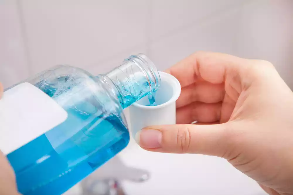 A person is holding a bottle of hand sanitizer, which can also be used as a sensitive teeth treatment.