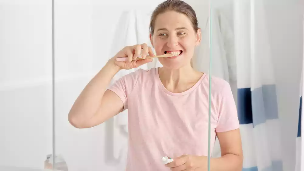 A woman post wisdom tooth extraction brushing her teeth in front of a mirror.
