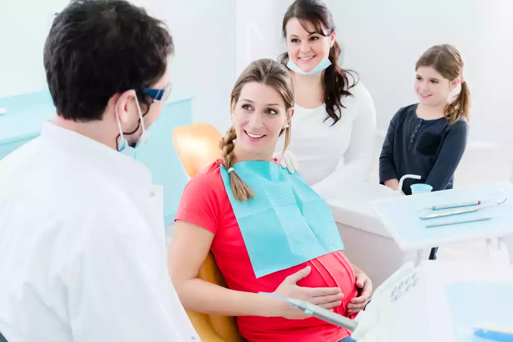 A pregnant woman is sitting in a dentist's chair, experiencing a toothache during pregnancy.