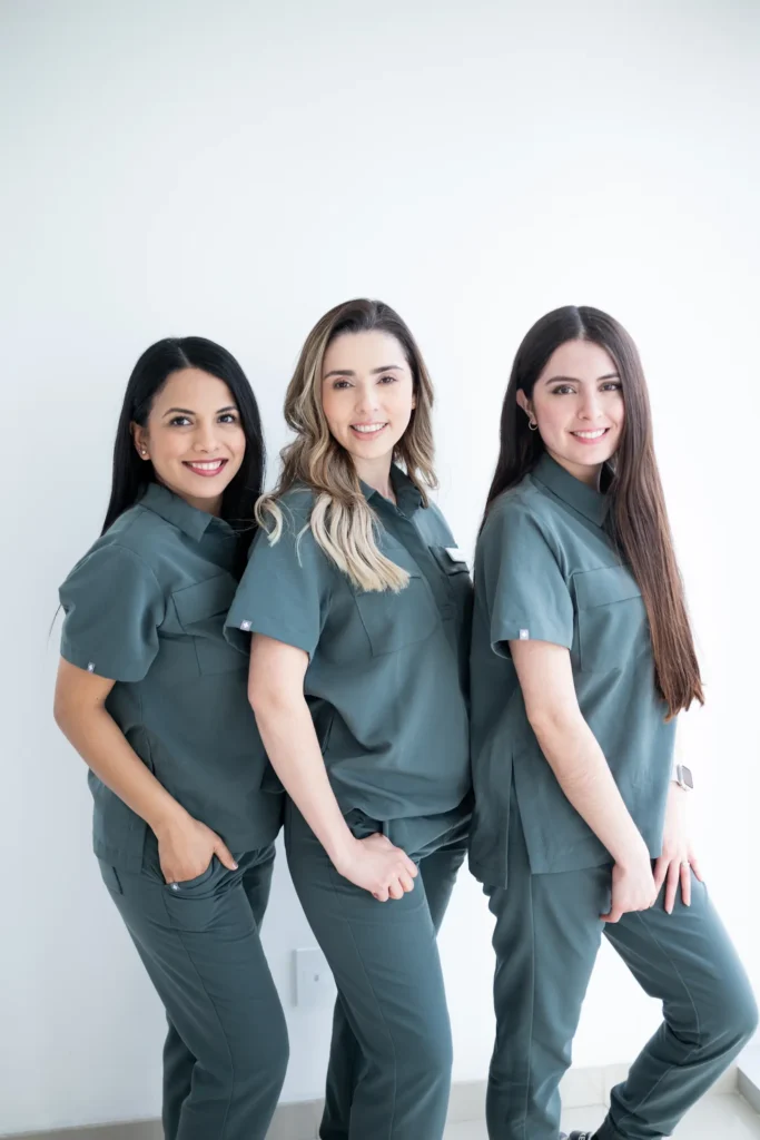 Three healthcare professionals in matching uniforms smiling and posing together.