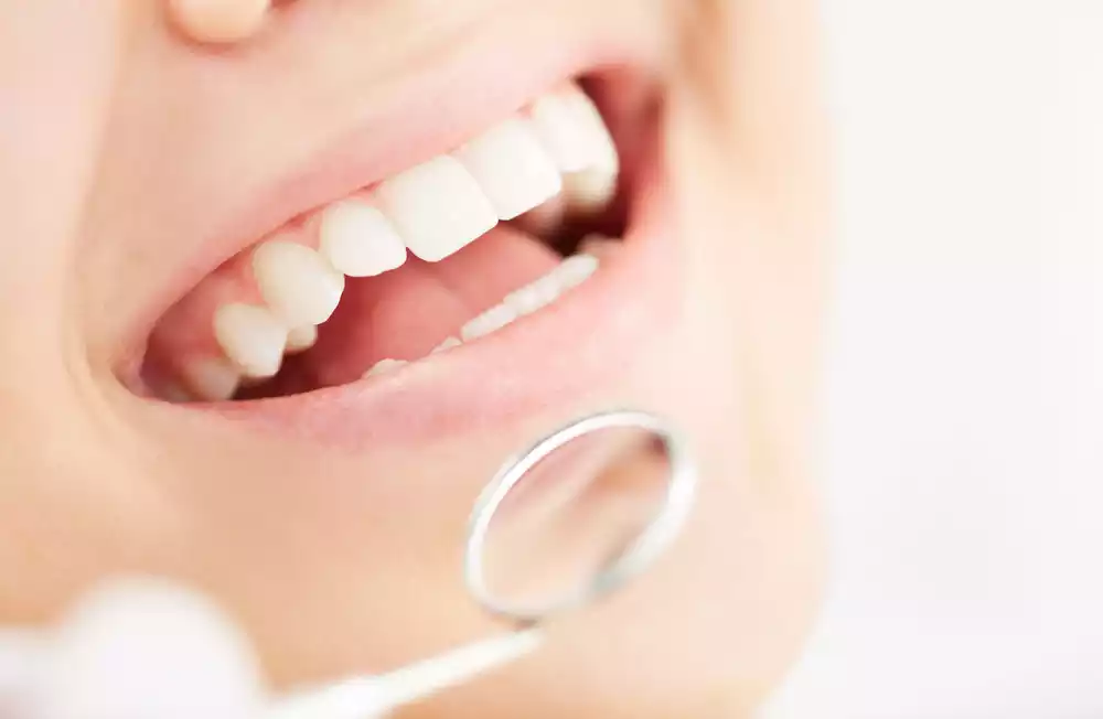 Close-up of a dentist examining a patient's teeth with a dental mirror. The patient's mouth is open, showing clean, white teeth, exemplifying excellent oral care essentials.