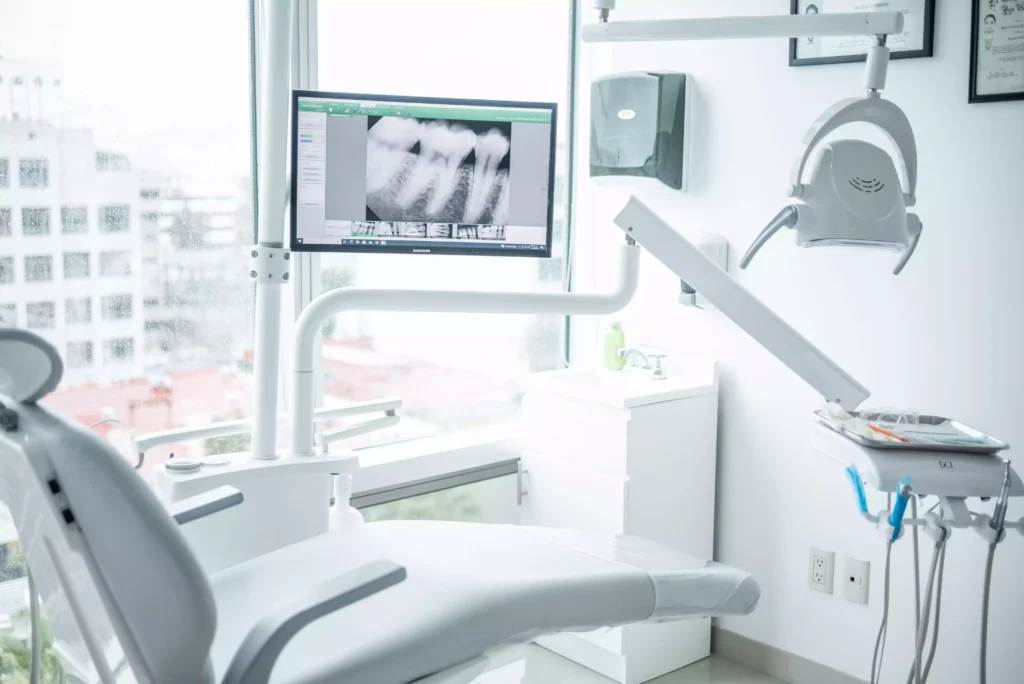 A modern dental office with a dentist chair, dental tools, and a computer screen displaying dental X-rays near a large window.
