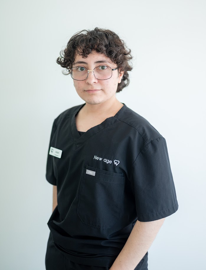 Person wearing glasses and black medical scrubs with a name tag and "New age" text on the pocket, standing against a plain light background.