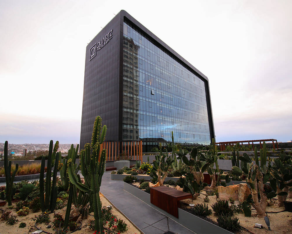 A modern glass office building labeled "Quartier" stands behind a landscaped garden with various cacti and desert plants.
