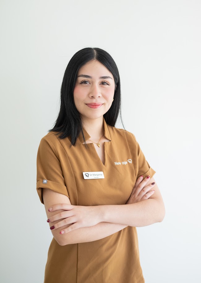 A woman with straight black hair stands against a white background, wearing a brown uniform with a name tag and her arms crossed, smiling slightly.