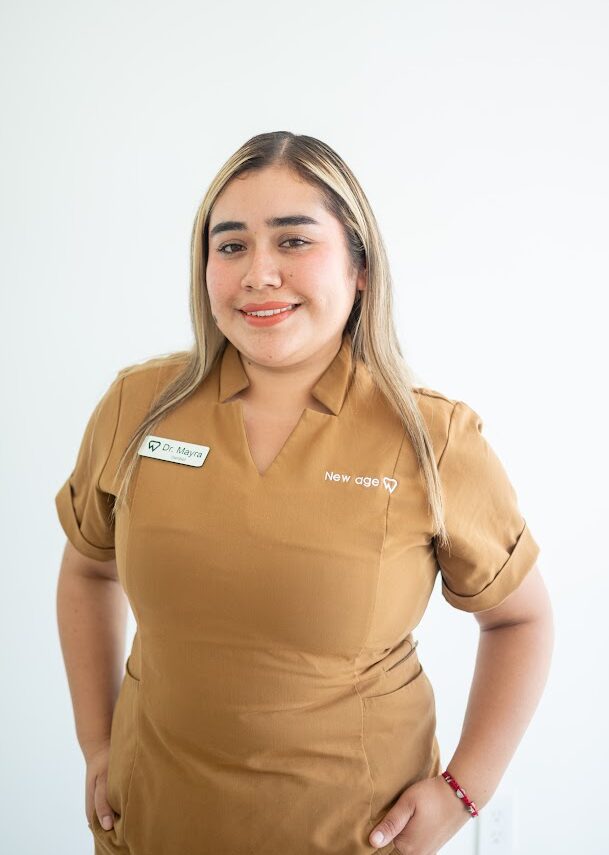 A woman wearing a brown uniform with a name tag that reads "Dr. Espin" stands in front of a plain white background, smiling at the camera.