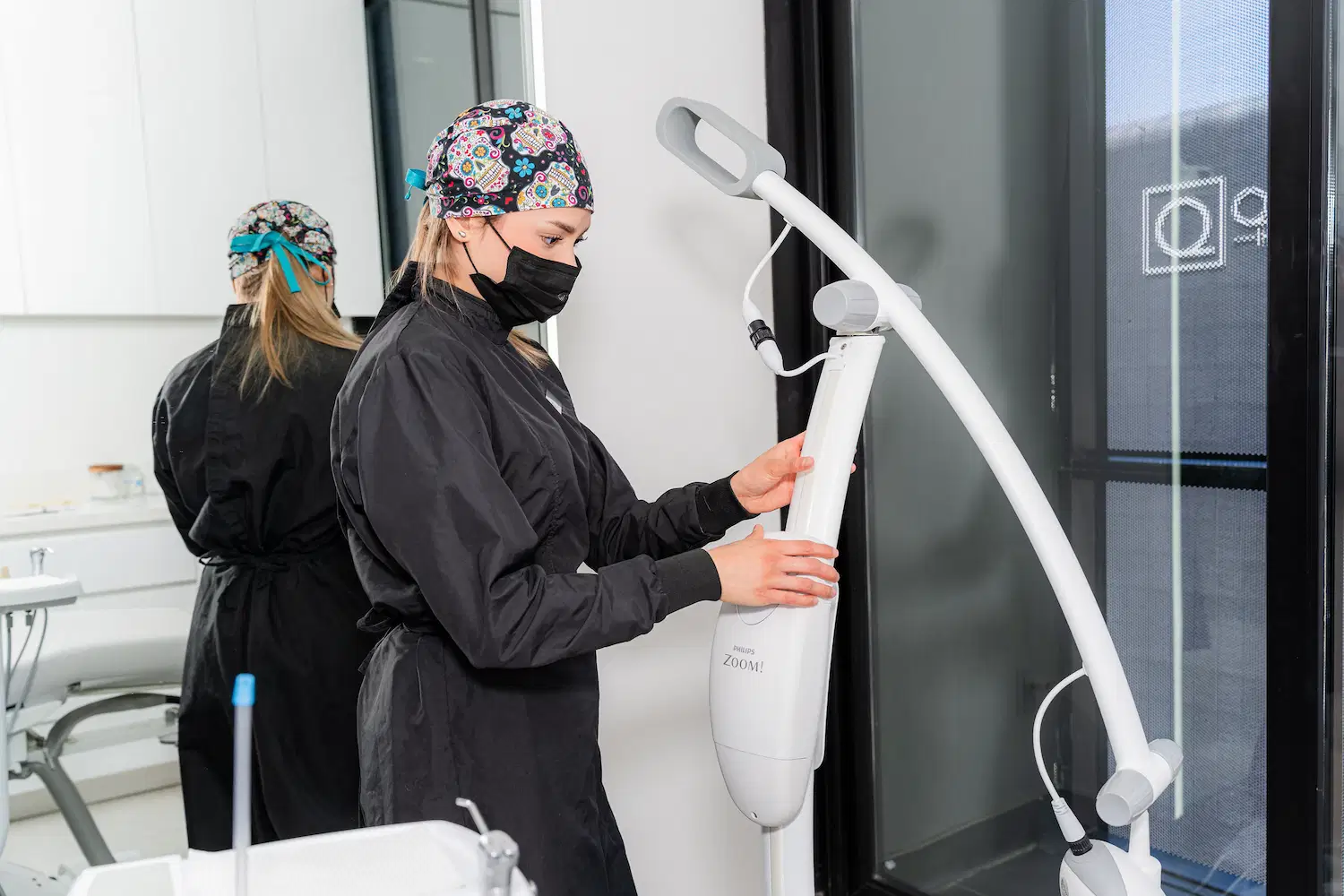A person in medical scrubs and a mask adjusts a dental or medical device in a clean, modern clinic room.