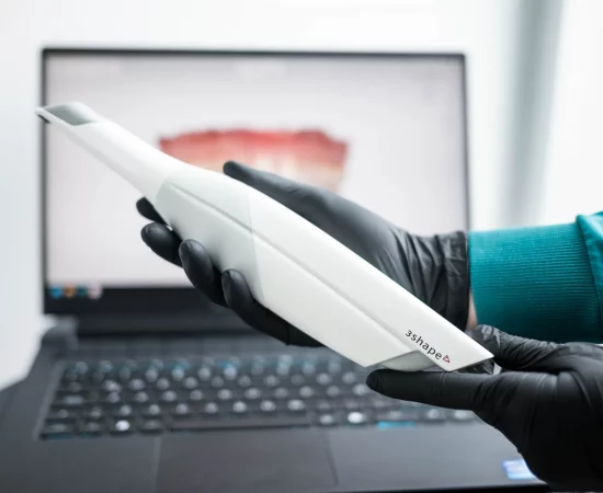 A person using a laptop for Digital Smile Design while holding a toothbrush.