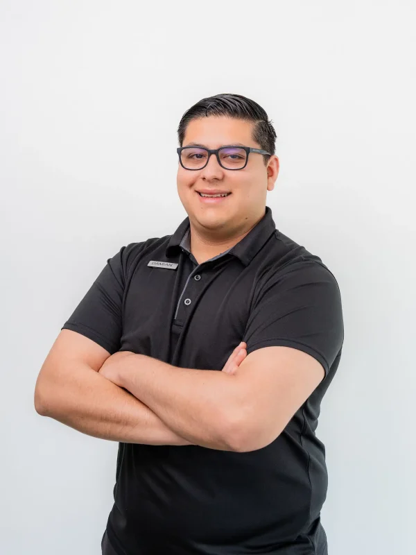 A man wearing glasses and a black polo shirt stands with arms crossed, smiling in front of a plain white background.