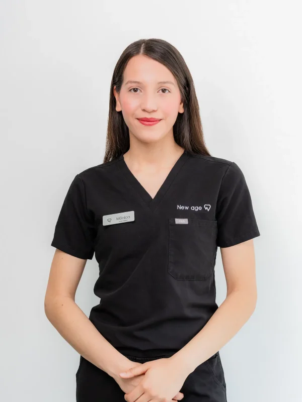 A woman in black medical scrubs with a name tag stands against a plain white background, hands clasped in front of her.