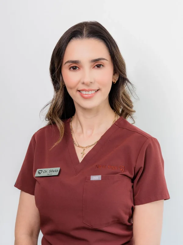 A woman in a maroon medical uniform with a name tag reading "Dr. Silvia" smiles at the camera against a plain white background.